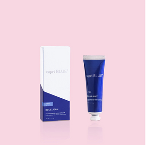 A mini hand cream tube next to its packaging box, both with the brand name 'capri BLUE' written on them, on a pink background.
