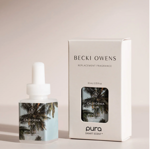 A product image featuring a white box with the brand name 'BECKI OWENS' and a replacement fragrance bottle with a palm tree design. The box is labeled 'California Sun' and indicates it is a part of the 'pura SMART SCENT' collection.