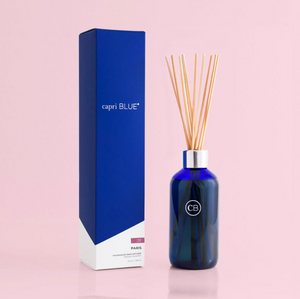 A blue reed diffuser with white tea, ginger, violets, and vanilla scents, alongside its blue packaging box with the brand name 'Capri Blue'.