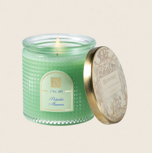 Green candle in a textured jar with a decorative lid on a beige background