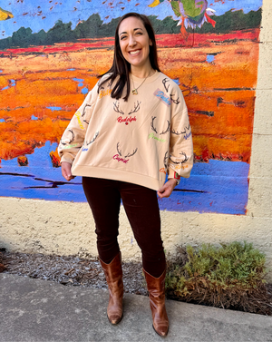 Woman wearing a beige sweater with reindeer designs in front of a colorful mural.