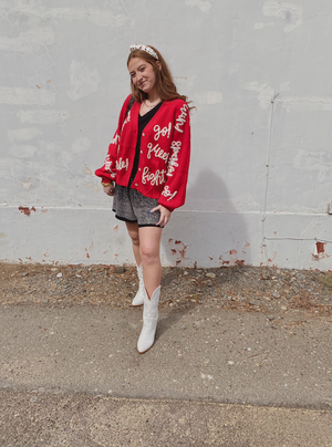 Individual wearing a red cardigan with text on it in front of a white wall.