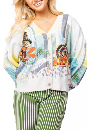Woman wearing a colorful kimono-style top with a nature-themed design and green striped pants.