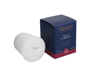 A white votive candle with a label reading 'Trapp No. 24 Wild Currant' in front of its blue packaging box.